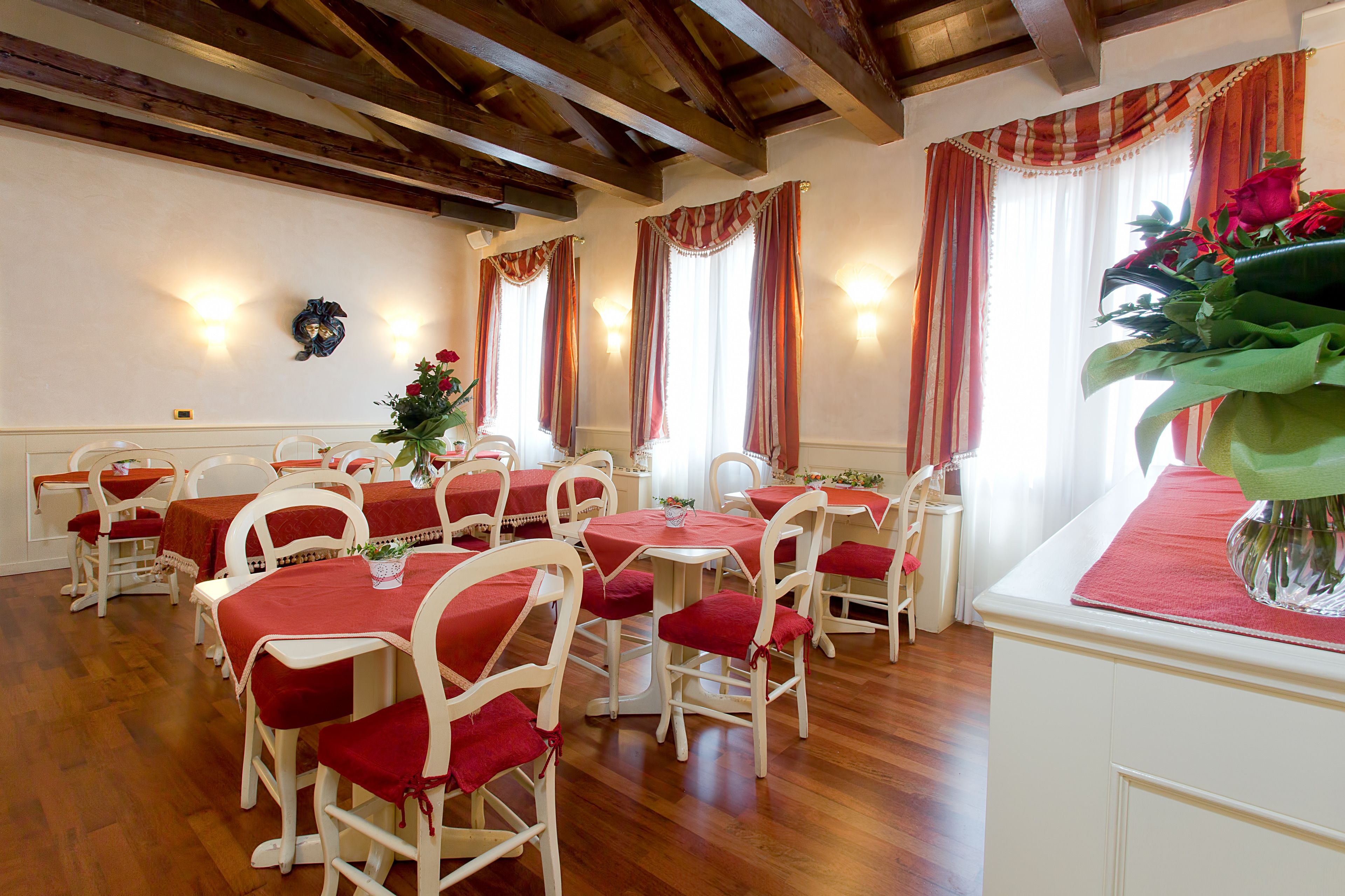 A dining area with wooden floors, white chairs, and tables covered with red tablecloths.