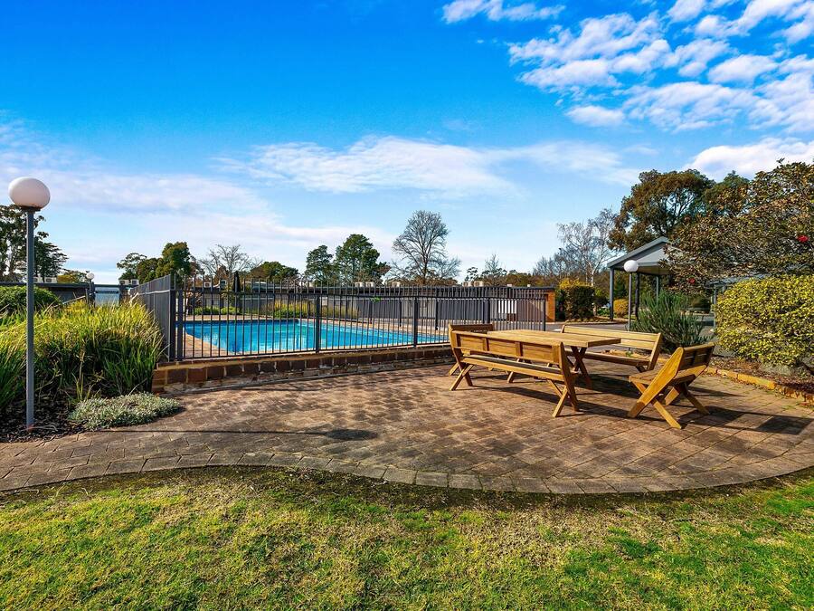 Un patio trasero con piscina, terraza de madera y un pabellón.