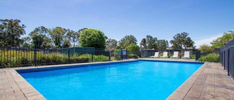 A rectangular swimming pool with a clear blue water surface, surrounded by a brick deck and a metal fence.