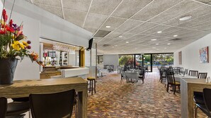 Un restaurante espacioso con suelo de baldosas, varias mesas y sillas, y una zona de bar con una exhibición de vinos.
