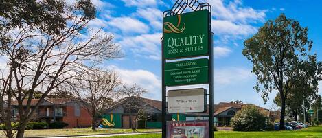 Un cartel de Quality Inn & Suites que destaca servicios como un bistró y cafetería con licencia, salón de conferencias, piscina, Wi-Fi gratuito y habitaciones renovadas.