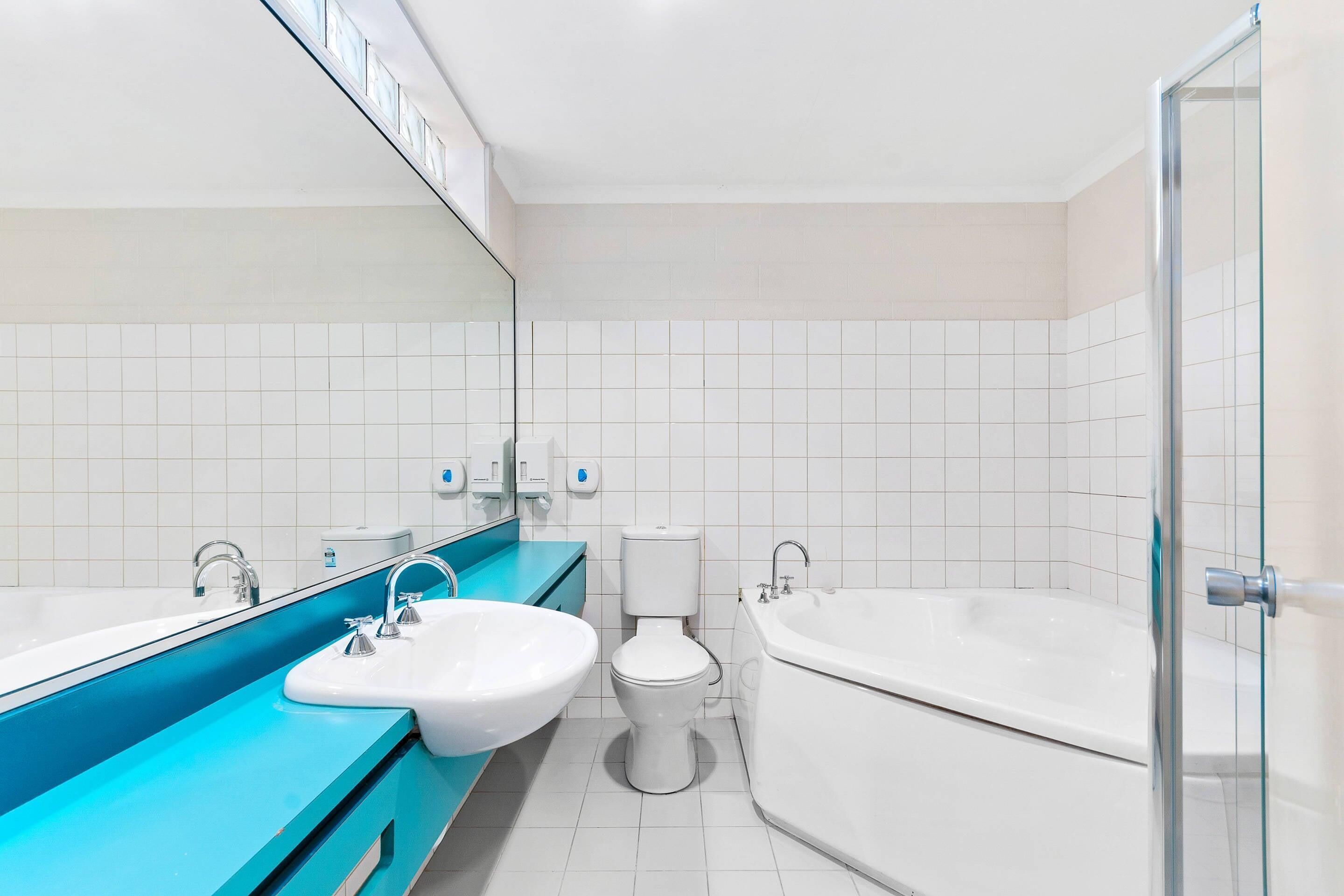 A modern bathroom with a large mirror, a sink, a toilet, and a bathtub.