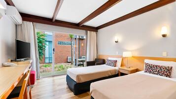 Quarto de hotel com duas camas, uma escrivaninha e uma televisão, além de uma porta de vidro que se abre para o exterior.