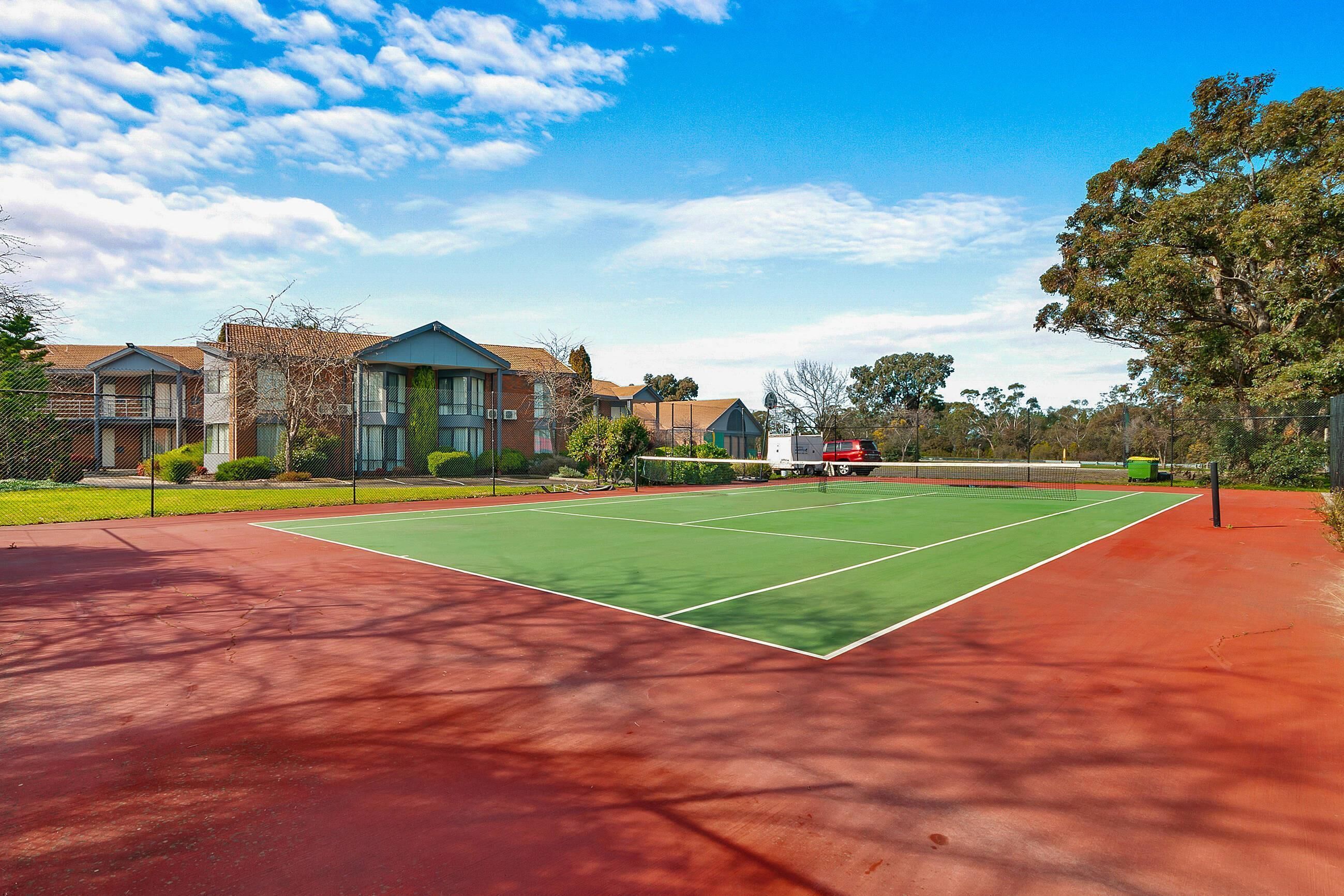 A tennis court with a red and green surface, surrounded by residential buildings and trees.