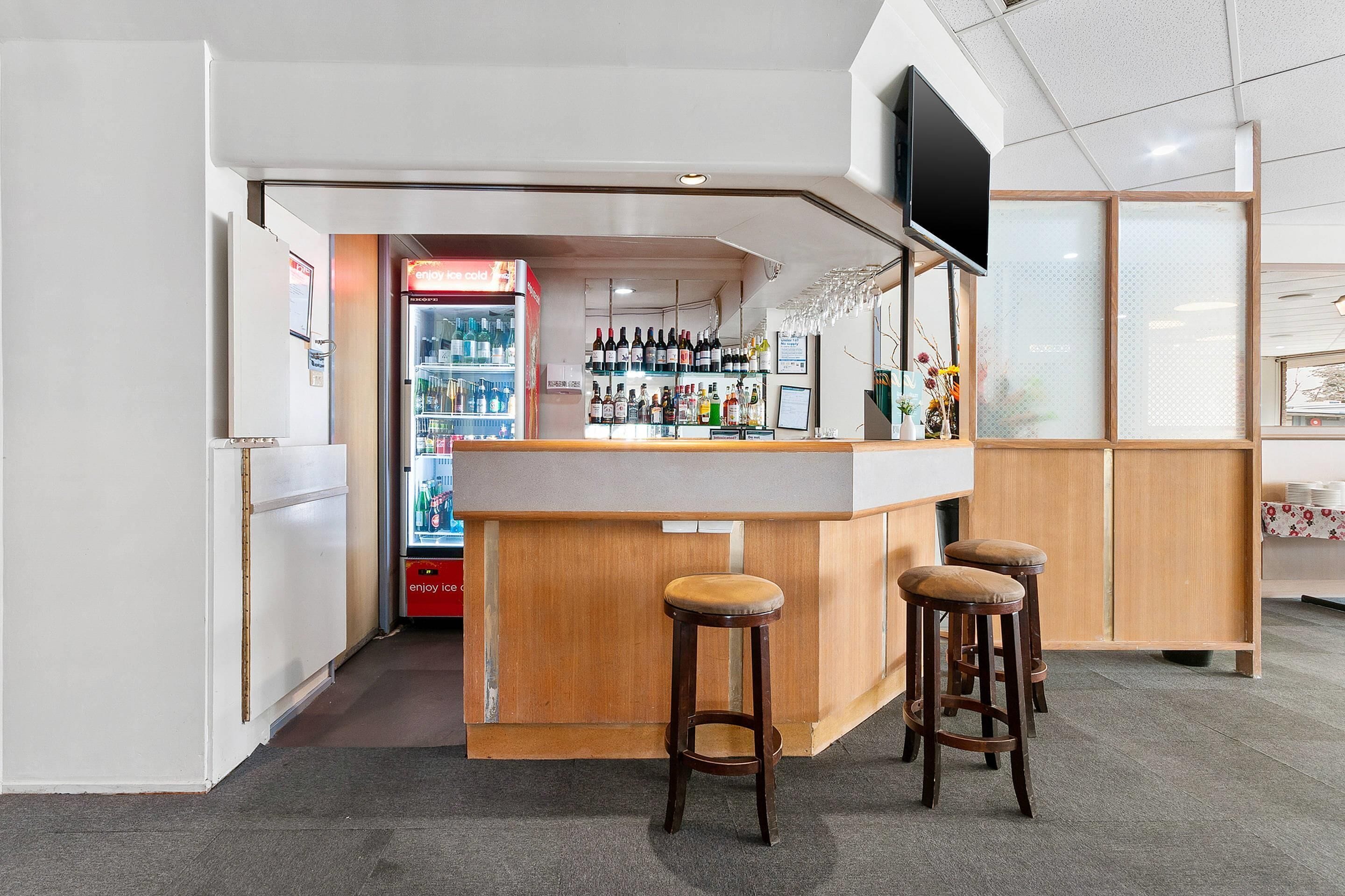 A bar area with stools, a refrigerator, and a shelf with bottles.
