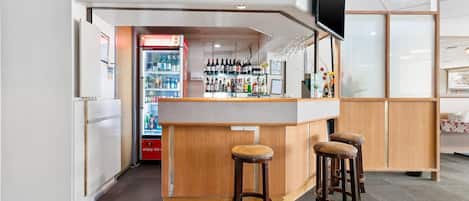 A bar area with stools, a refrigerator, and a shelf with bottles.