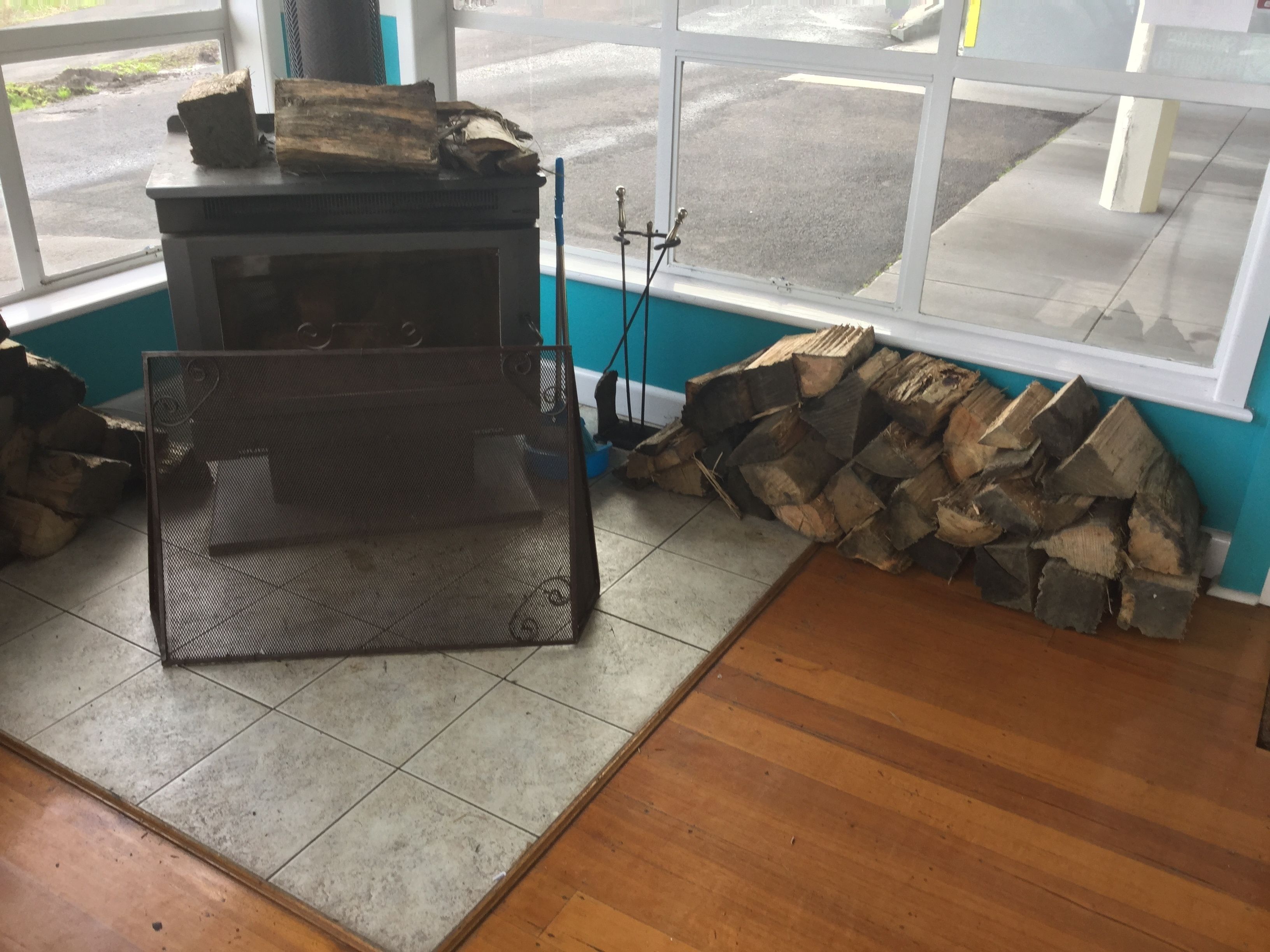 A room with a wood-burning stove, a metal screen, and a stack of firewood.