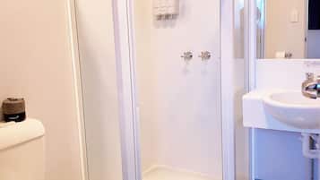 Et badeværelse med en glasafskærmet brusekabine, toilet og håndvask.