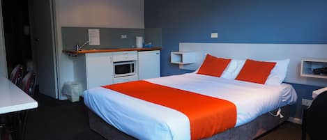 A hotel room with a bed, a microwave, a small desk, and a chair.
