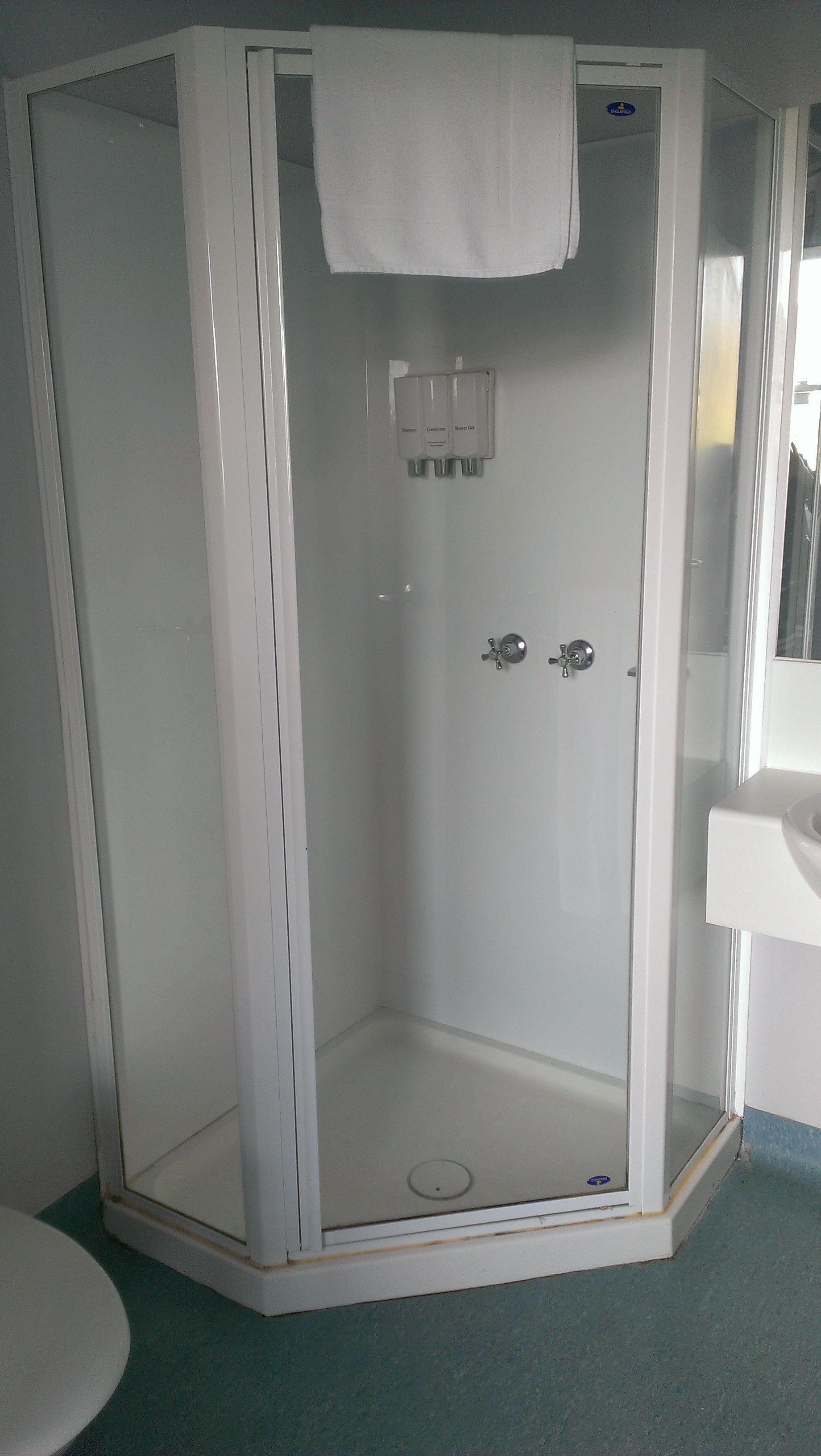 Eine weiße, gläserne Dusche mit einem weißen Handtuch, das an der Tür hängt.