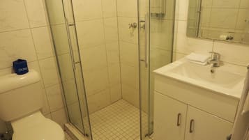 Kylpyhuoneessa on lasiseinällä varustettu suihku, wc ja pesuallas, jonka yläpuolella on peili.