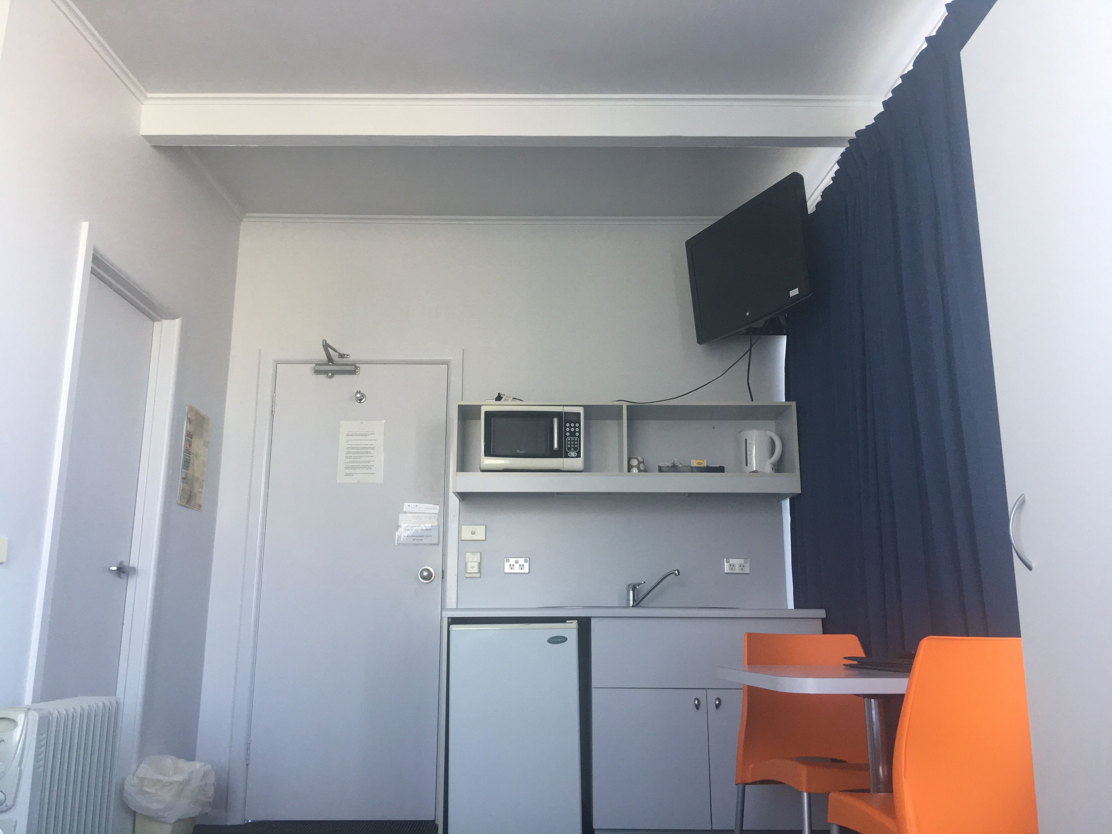 Una kitchenette compacta con microondas, un refrigerador pequeño, un lavamanos y una mesa con dos sillas anaranjadas.