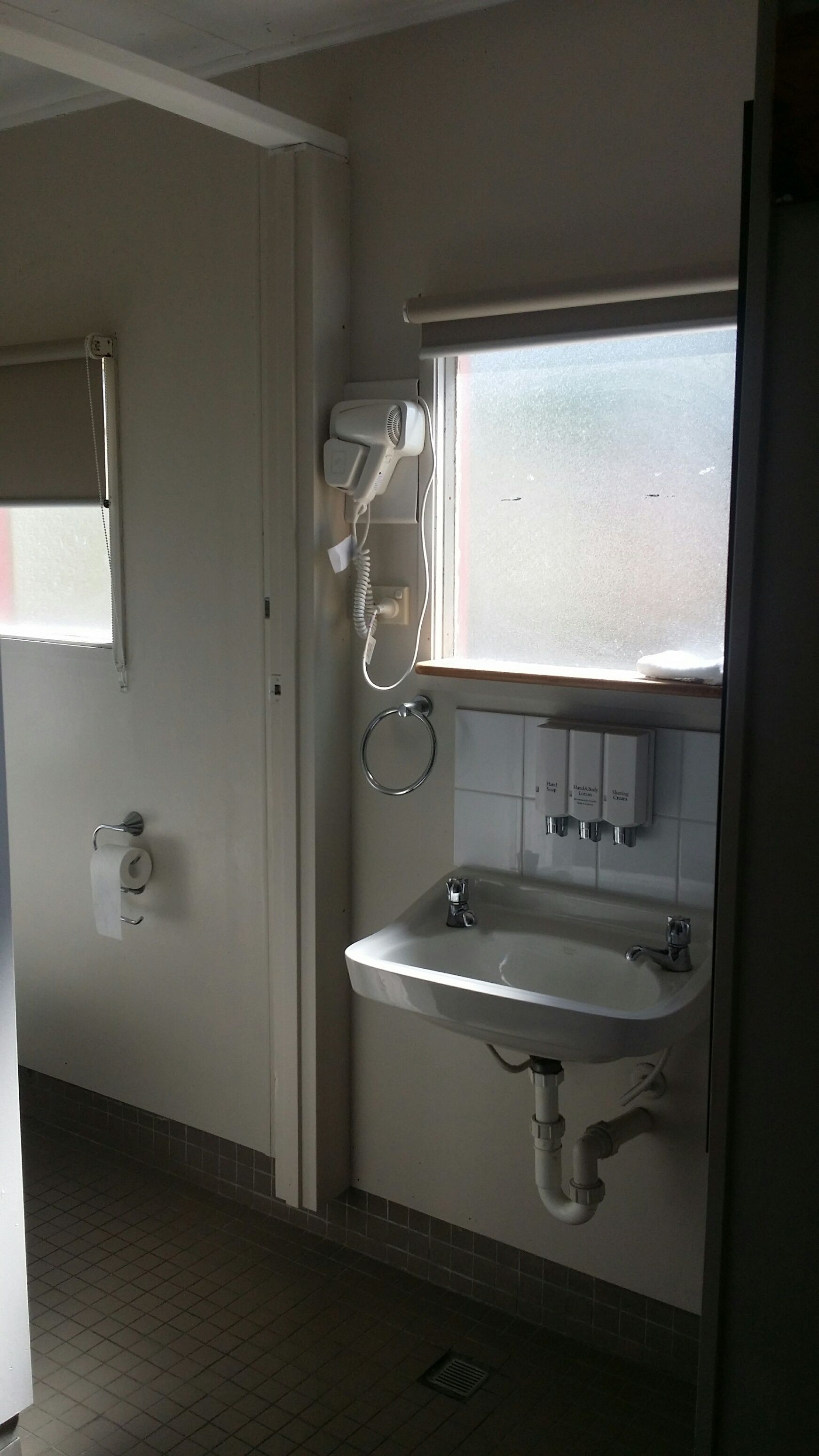 A bathroom with a sink, a hand dryer, a towel ring, and a window.