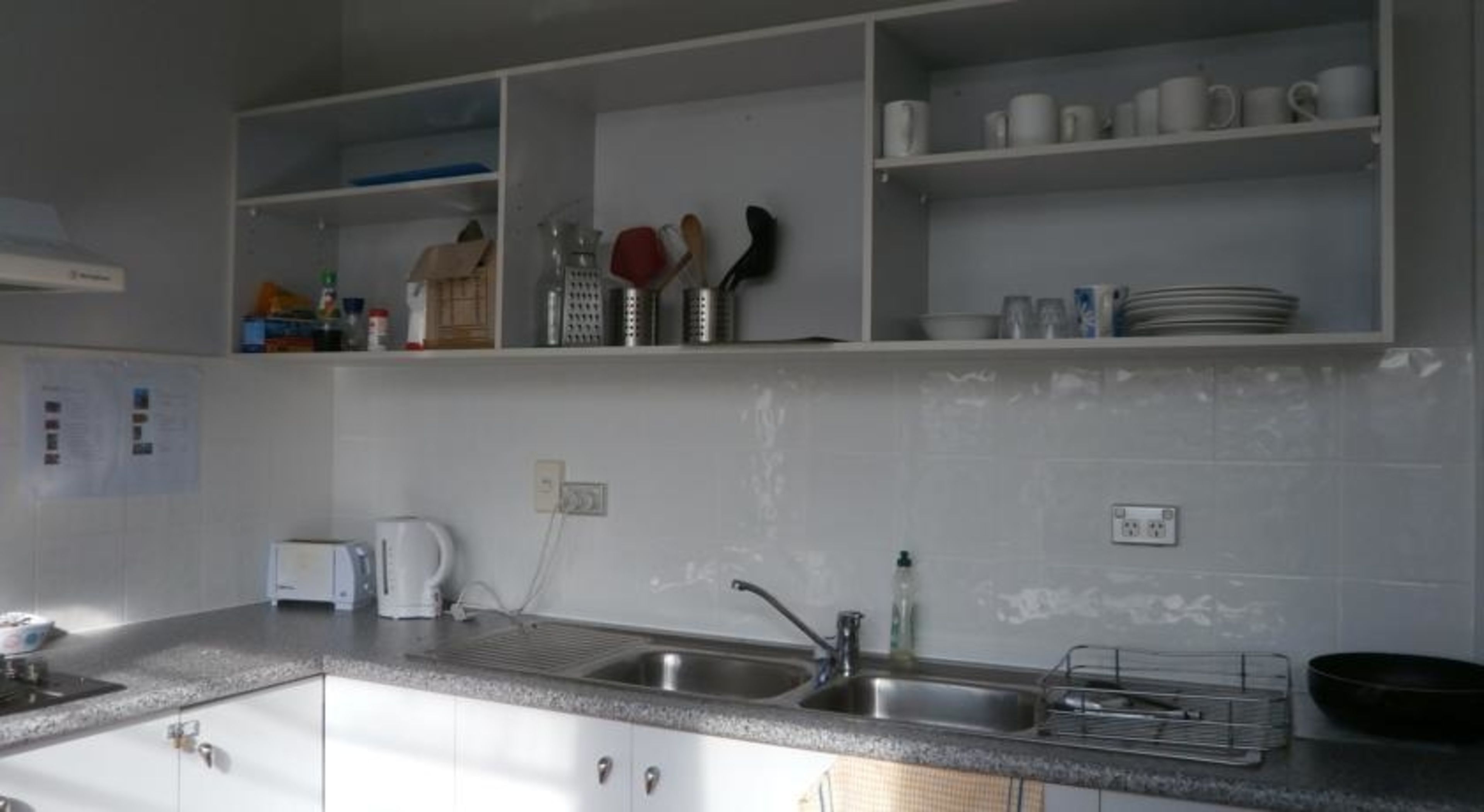A kitchen with white cabinets, a sink, a kettle, and various utensils on shelves.