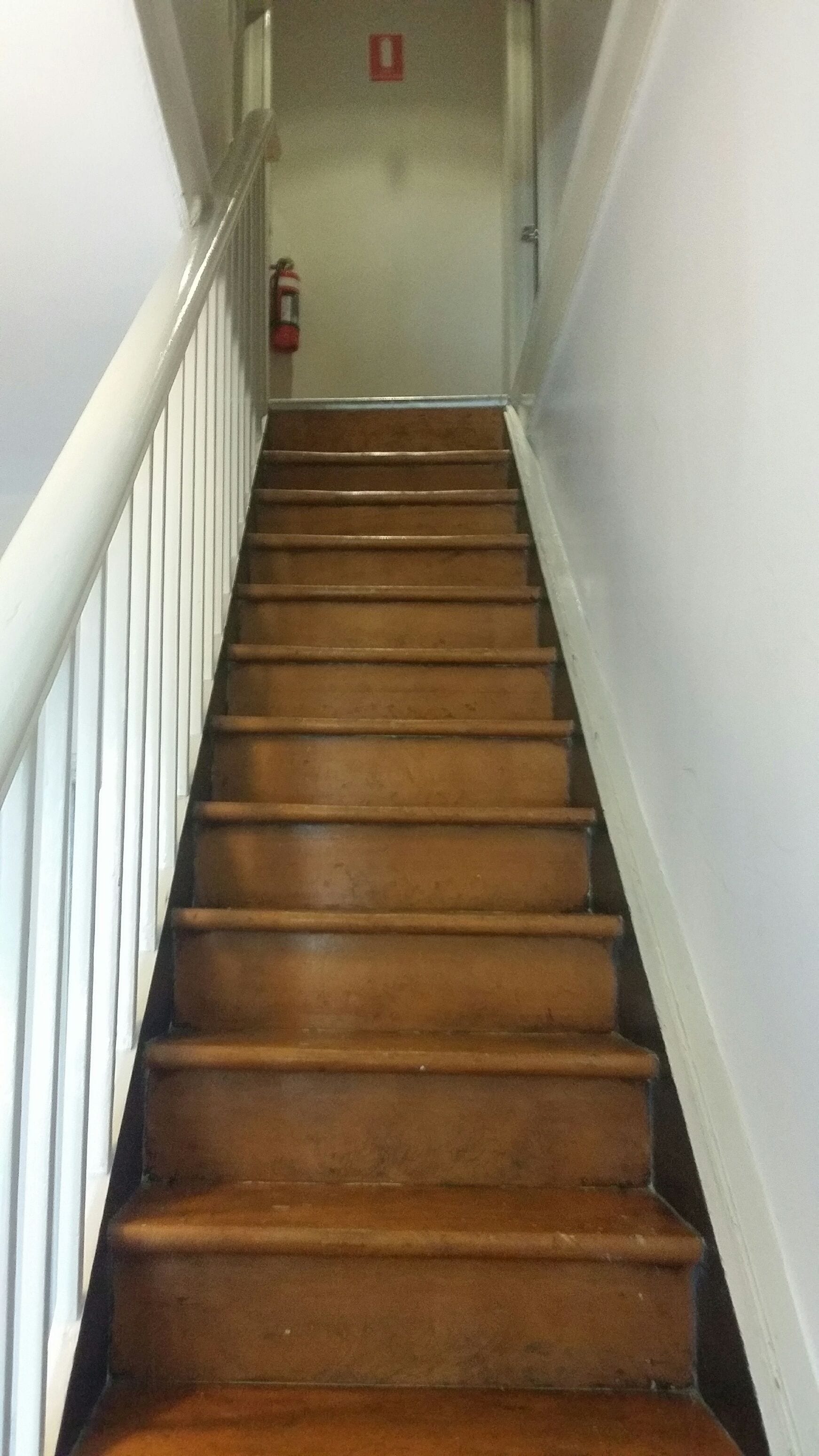 A wooden staircase with white railings, leading to a landing with a fire extinguisher mounted on the wall.