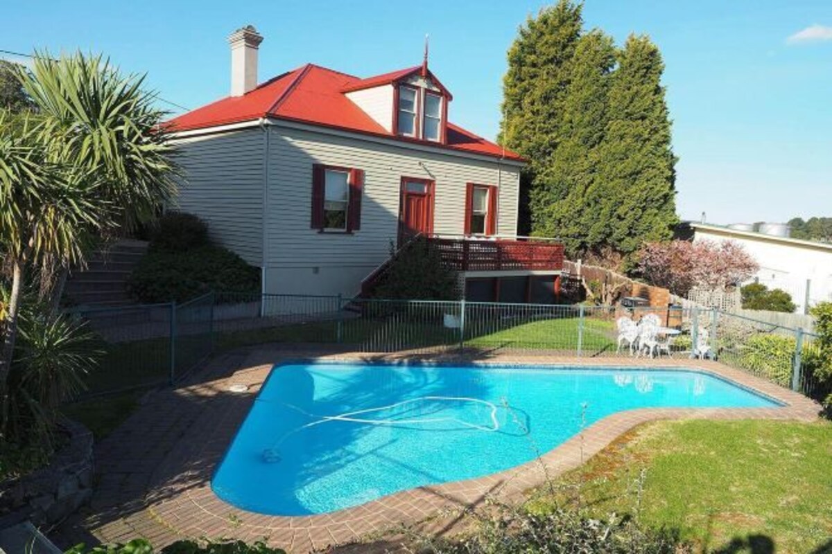 A house with a swimming pool, a red roof, and a fenced yard.