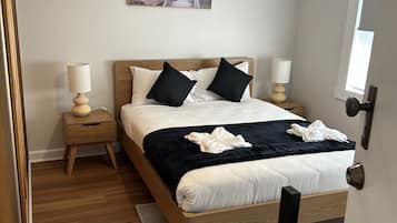Een slaapkamer met een houten bed, twee nachtkastjes met lampen, een schilderij aan de muur en een airconditioning.