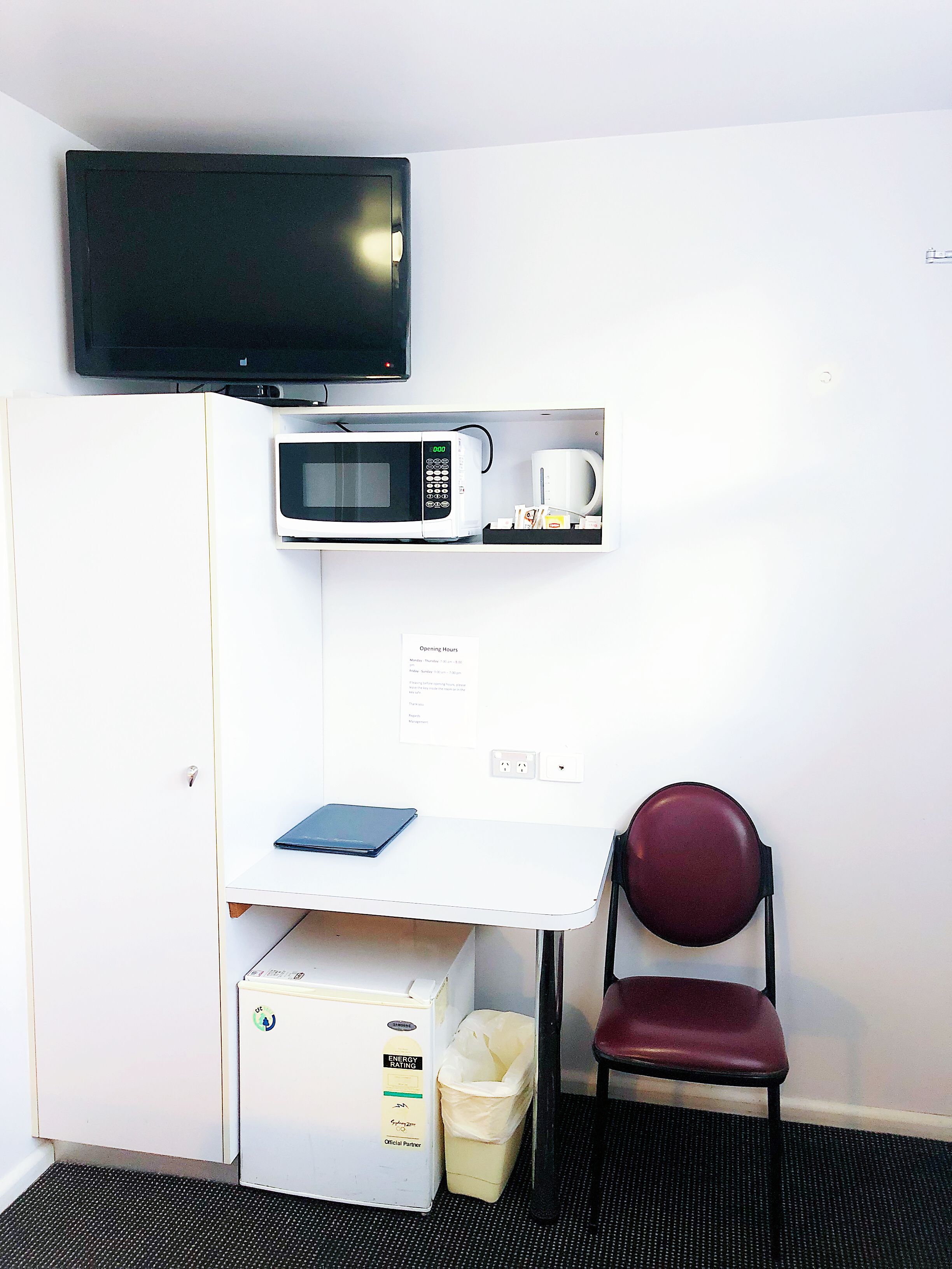 Quarto compacto com televisão, micro-ondas e uma pequena mesa com um laptop.