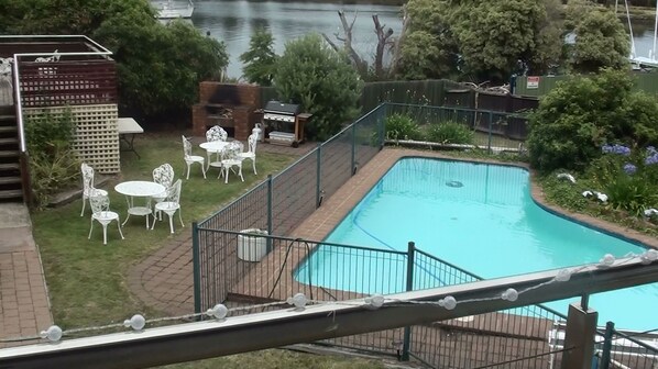 Una piscina con un deck alrededor, un área de barbacoa y mobiliario de exterior.