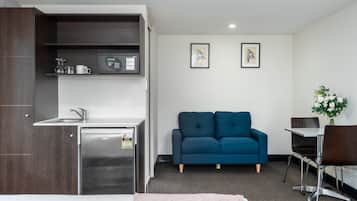 Ein kompaktes Hotelzimmer mit Küchenzeile, einer Couch, einem kleinen Tisch und einem Bett.