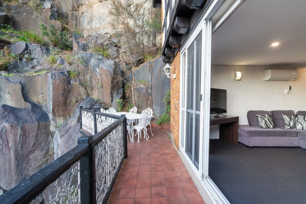 A balcony with a stone wall, a dining table with chairs, and a sofa inside a room with an air conditioner. - Leisure Inn Penny Royal Hotel & Apartments (Launceston)