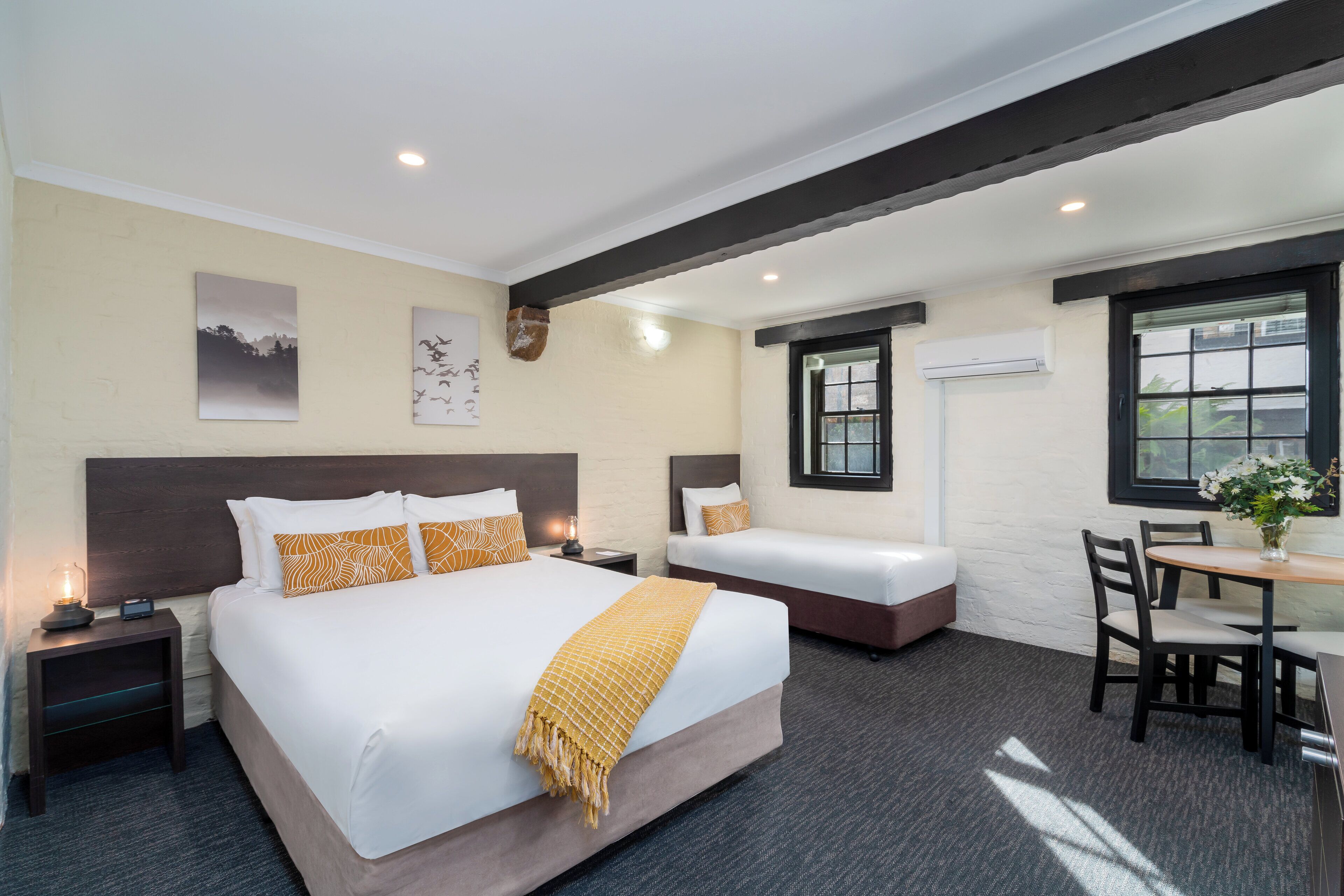 A hotel room with a large bed, a smaller bed, a desk with chairs, and artwork on the walls.