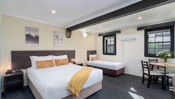 A hotel room with a large bed, a smaller bed, a desk with chairs, and artwork on the walls.