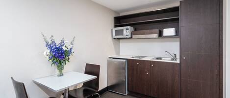 A compact kitchen with a microwave, toaster, and sink. There is a dining table with chairs and a vase of flowers.