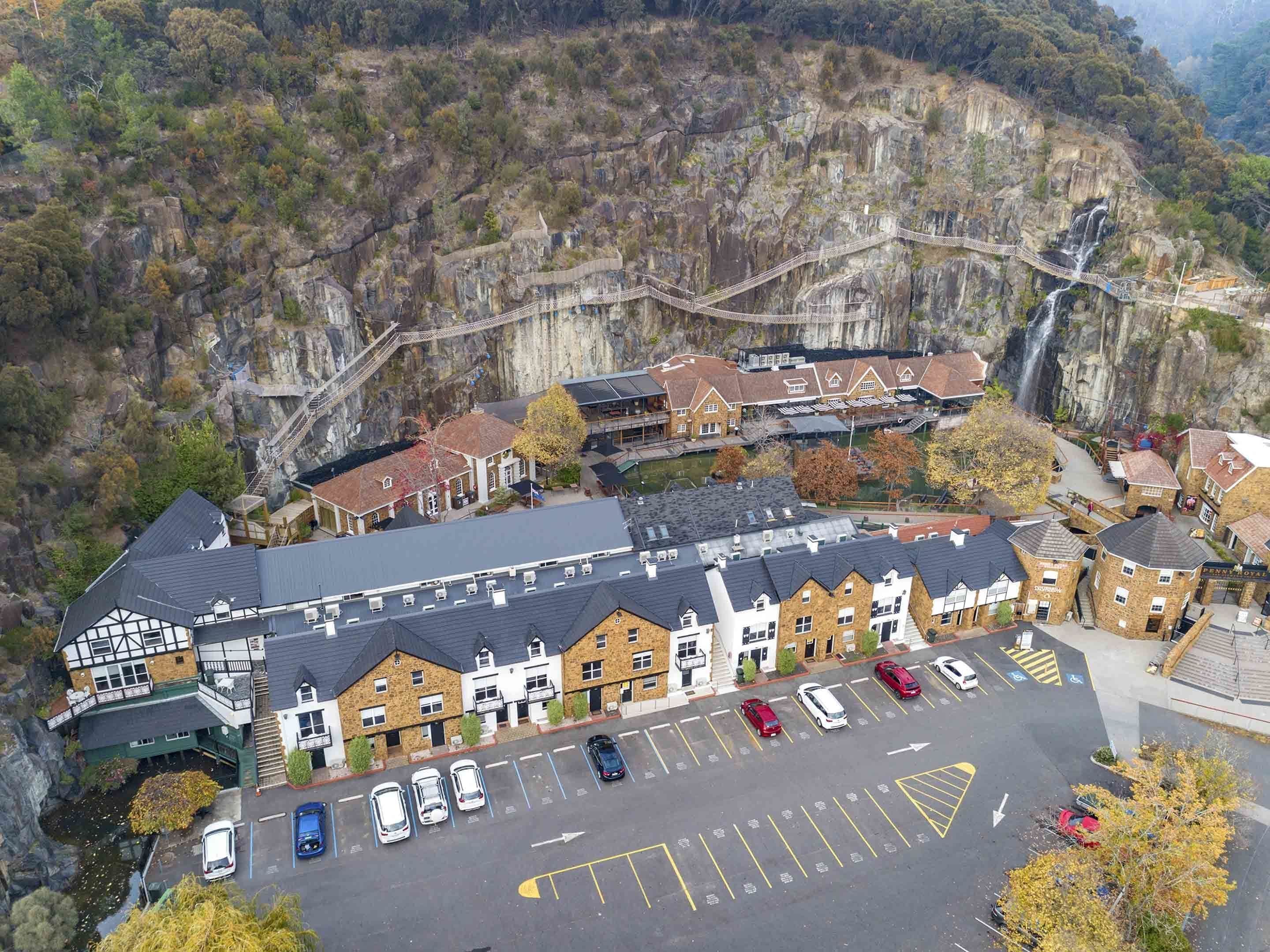 Een hotel met een traditionele architectuur, met een gevel van natuursteen en meerdere verdiepingen. Het bevindt zich in een bergachtig gebied met uitzicht op een waterval en een hangbrug.