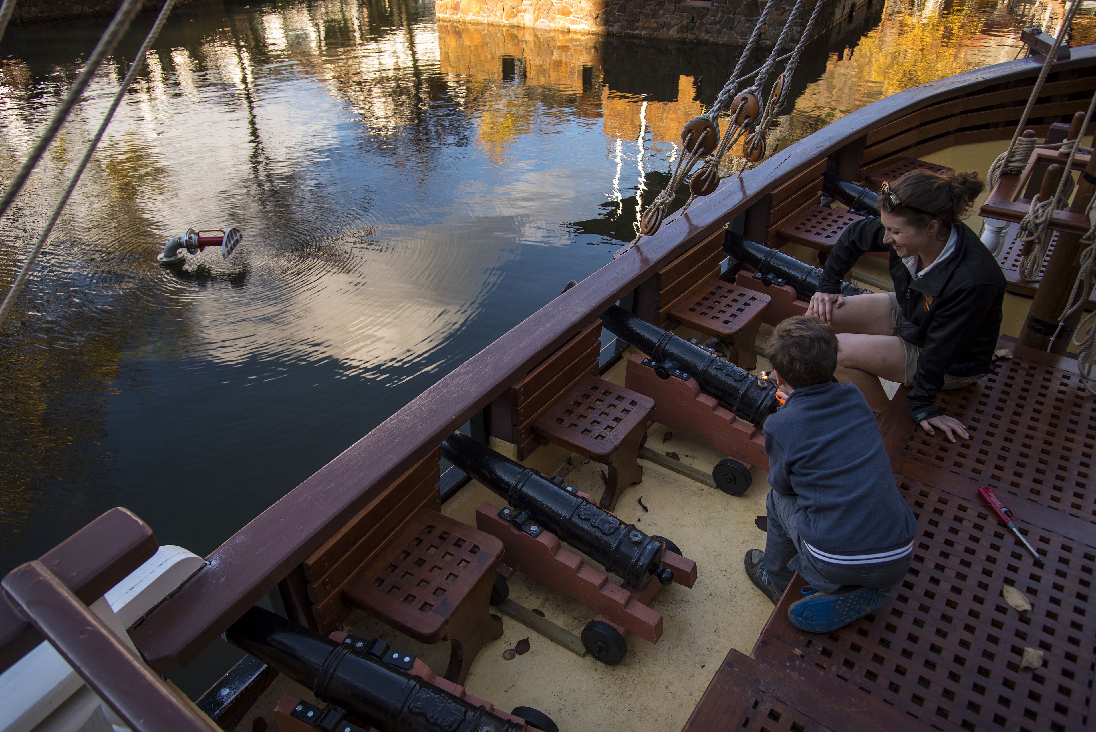 A model ship with cannons on deck, a person operating a cannon, and a child observing.
