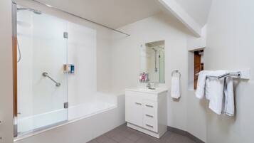 Une salle de bain moderne avec une douche à parois de verre, un meuble-lavabo blanc doté de tiroirs, un miroir et un porte-serviettes.