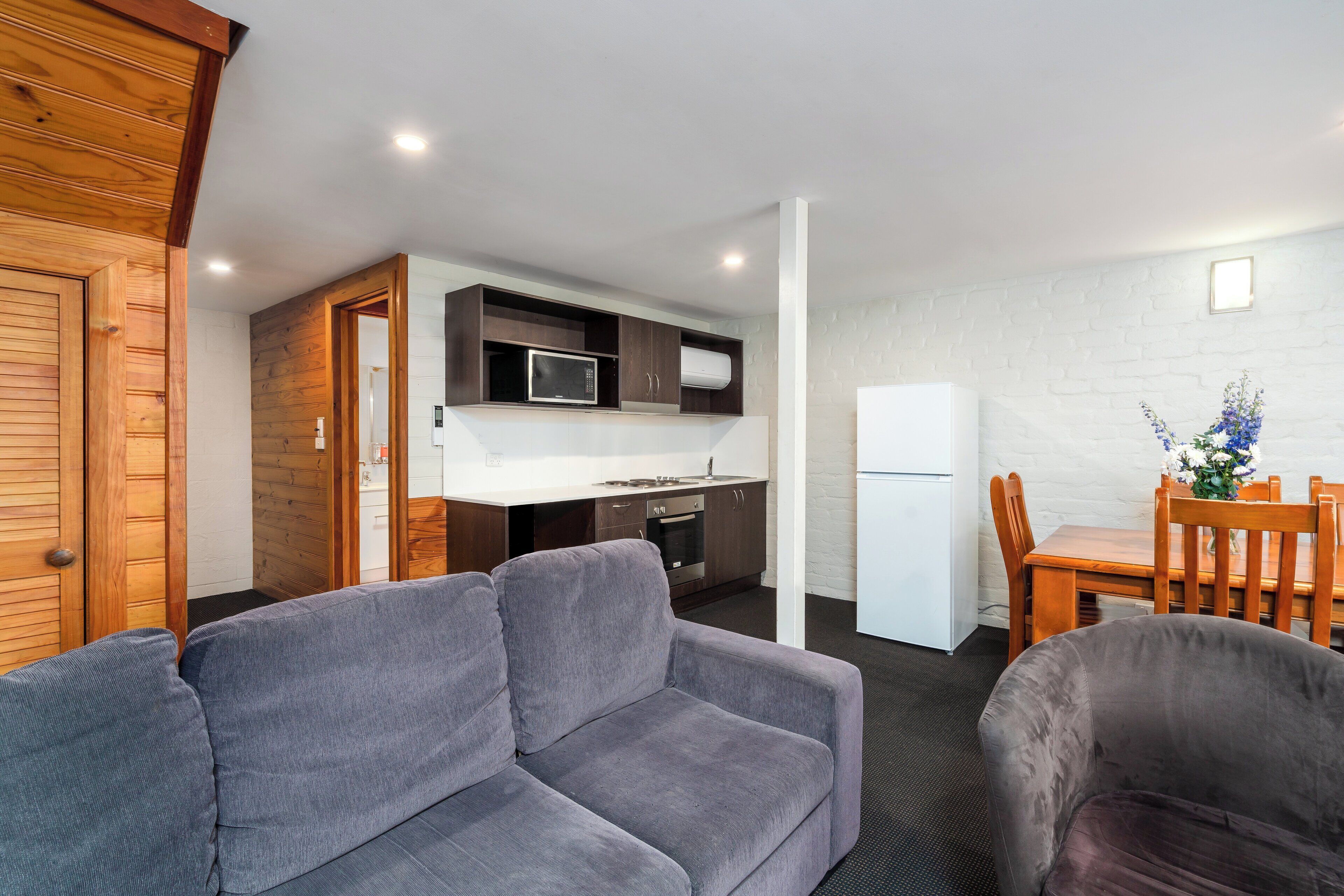 A compact living space with a kitchenette, grey sofa, dining table, and chairs.