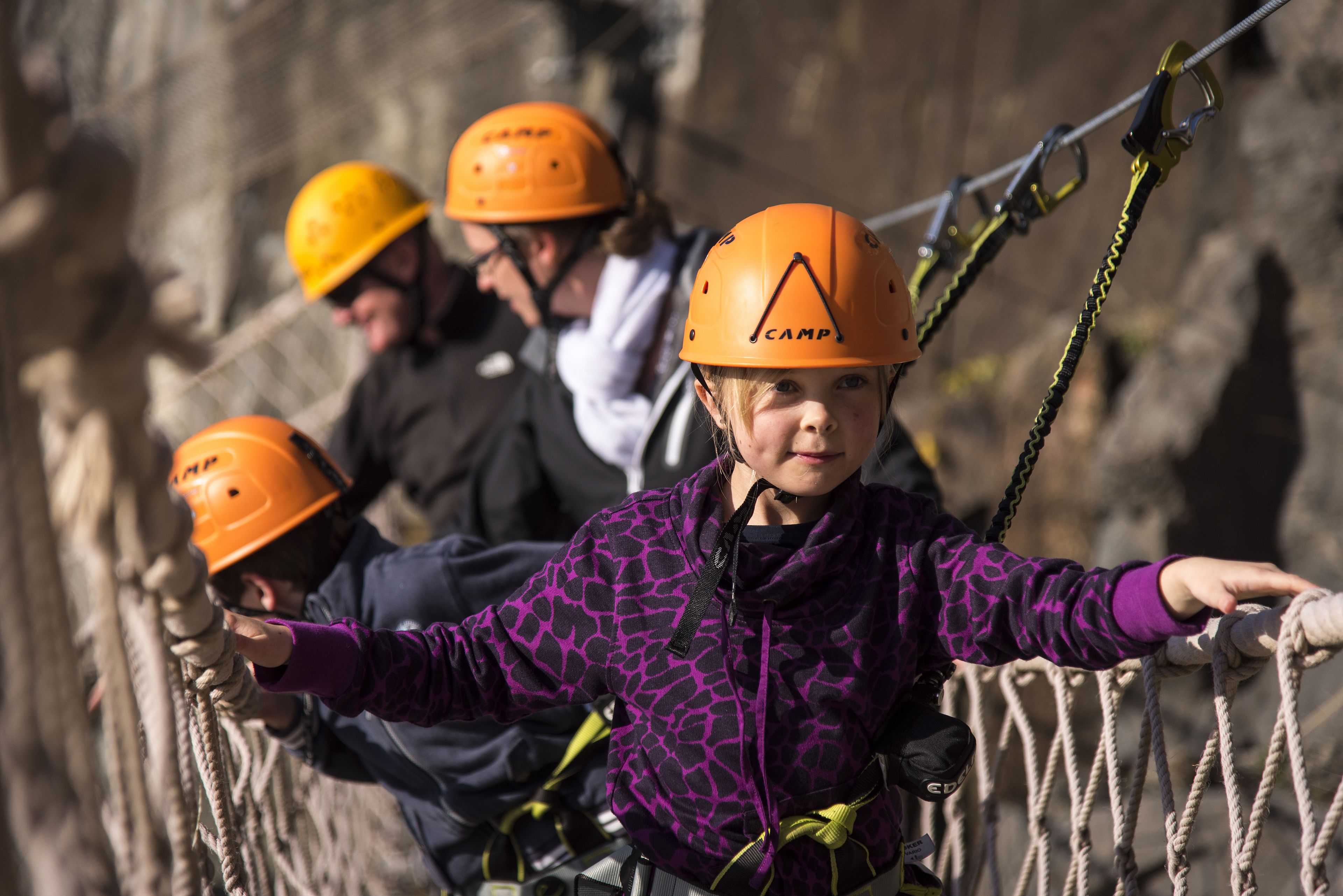 A person wearing a helmet with the word "CAMP" on it, standing on a rope bridge.