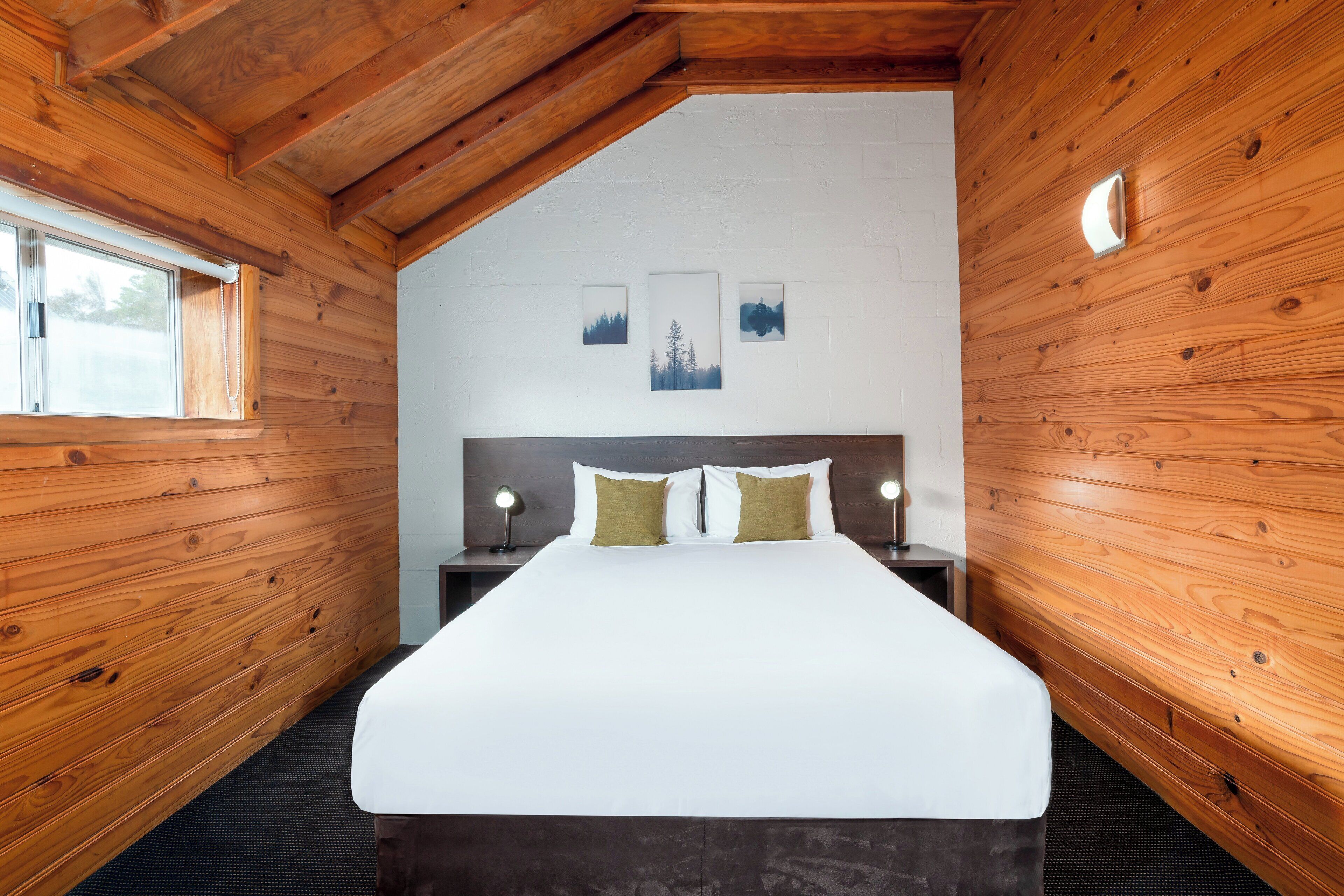 A bedroom with a large bed, wooden walls, a sloped ceiling, and framed pictures on the wall.