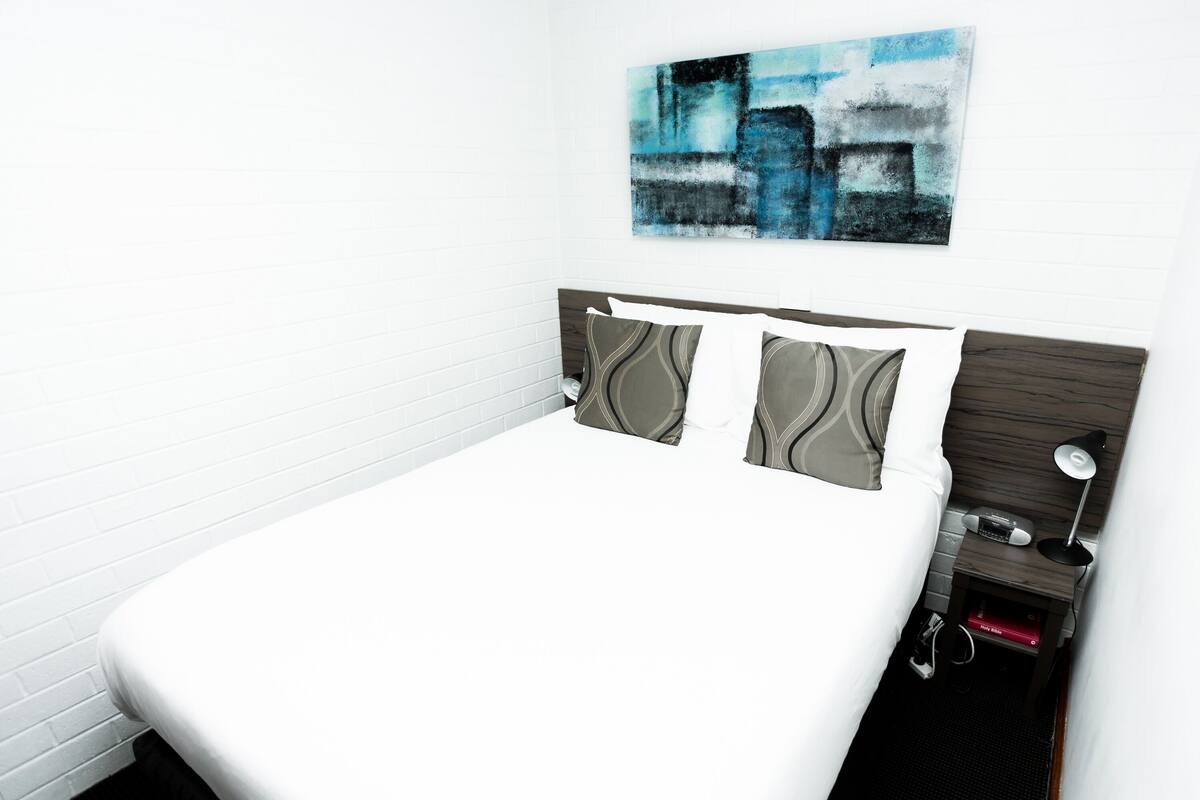 A neatly made bed with a white sheet, a headboard with a dark wood finish, and three pillows with a gray and white pattern.