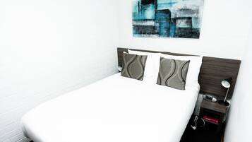 A neatly made bed with a white sheet, a headboard with a dark wood finish, and three pillows with a gray and white pattern.