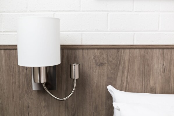 A wall-mounted lamp with a cylindrical shade and a flexible neck, mounted on a wooden panel with a white brick wall in the background. - Bay Hotel Apartments (Sandy Bay)