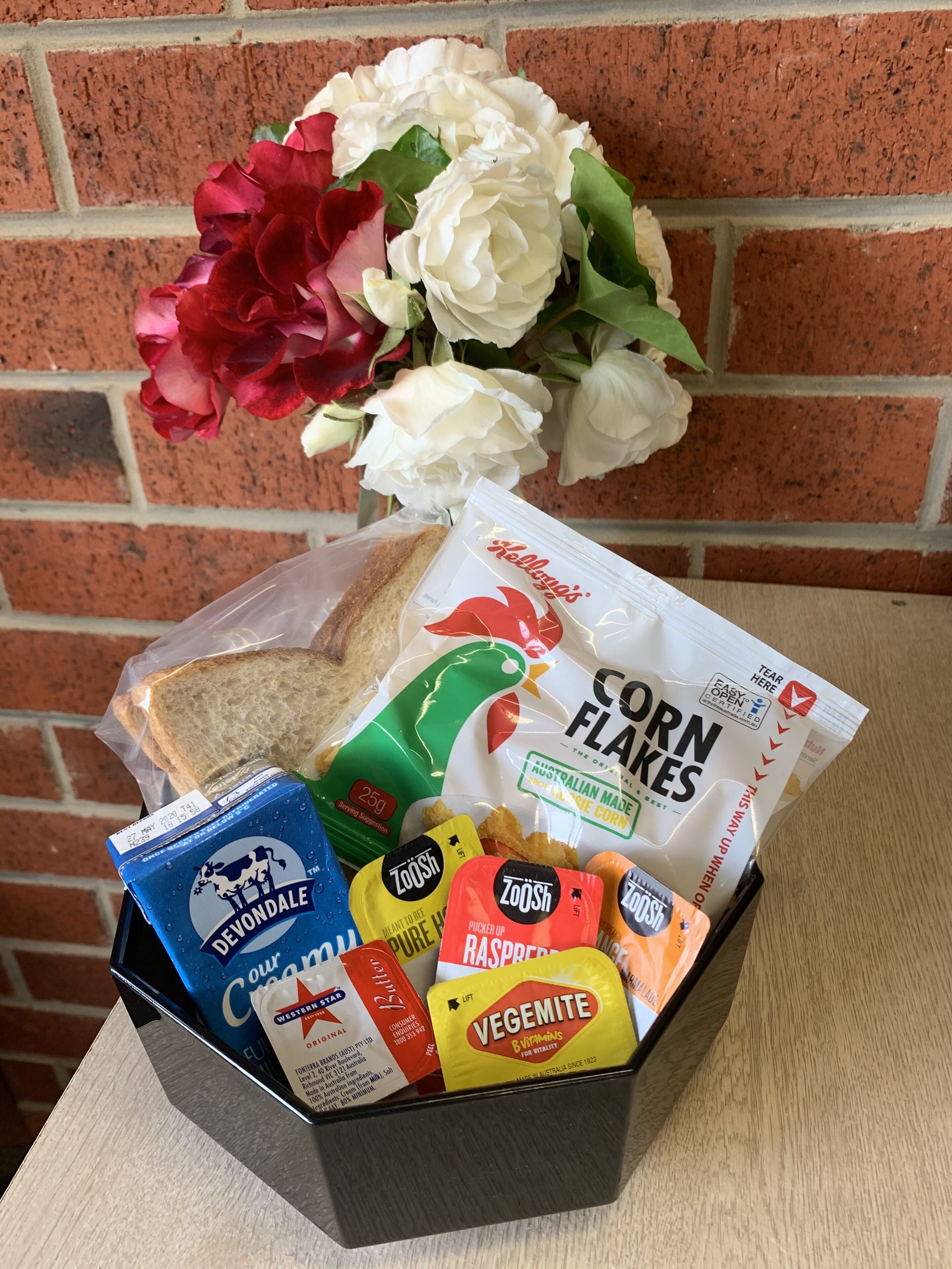 A gift basket with bread, corn flakes, Vegemite, and a bouquet of flowers.