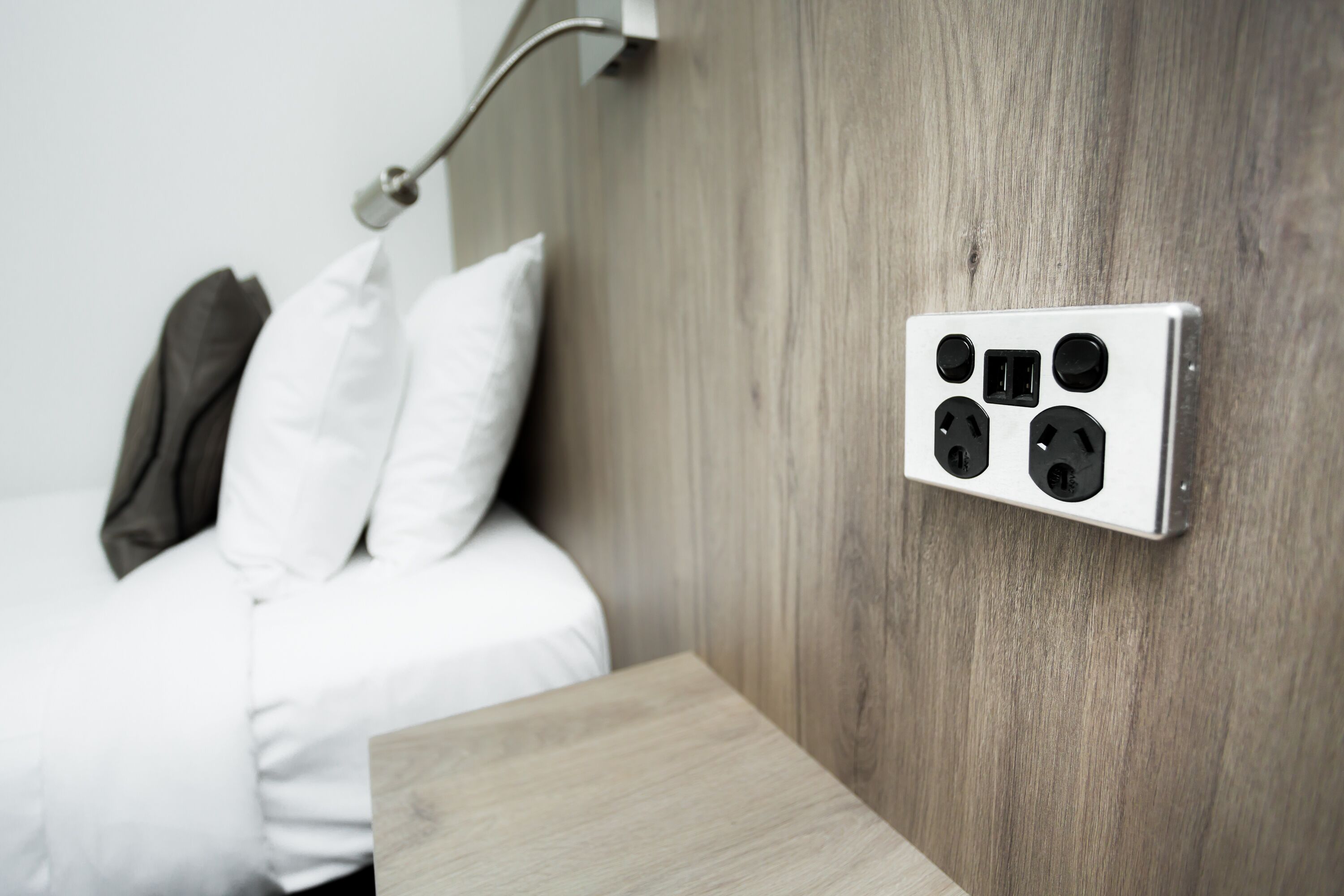 Un dormitorio moderno con cabecera de madera, una mesita de noche y un enchufe en la pared.