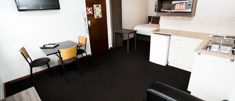 Een compacte hotelkamer met een flatscreen-tv, een zithoek met een tafel en stoelen, een kitchenette met een magnetron, en een klein zithoekje met een bank.