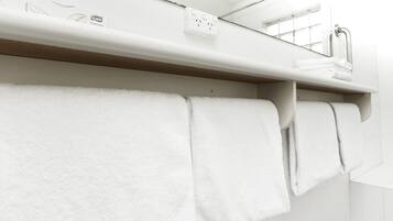 Un baño con toallas blancas colgadas en un perchero, un espejo sobre el lavabo y una salida TORK Premium en la pared.