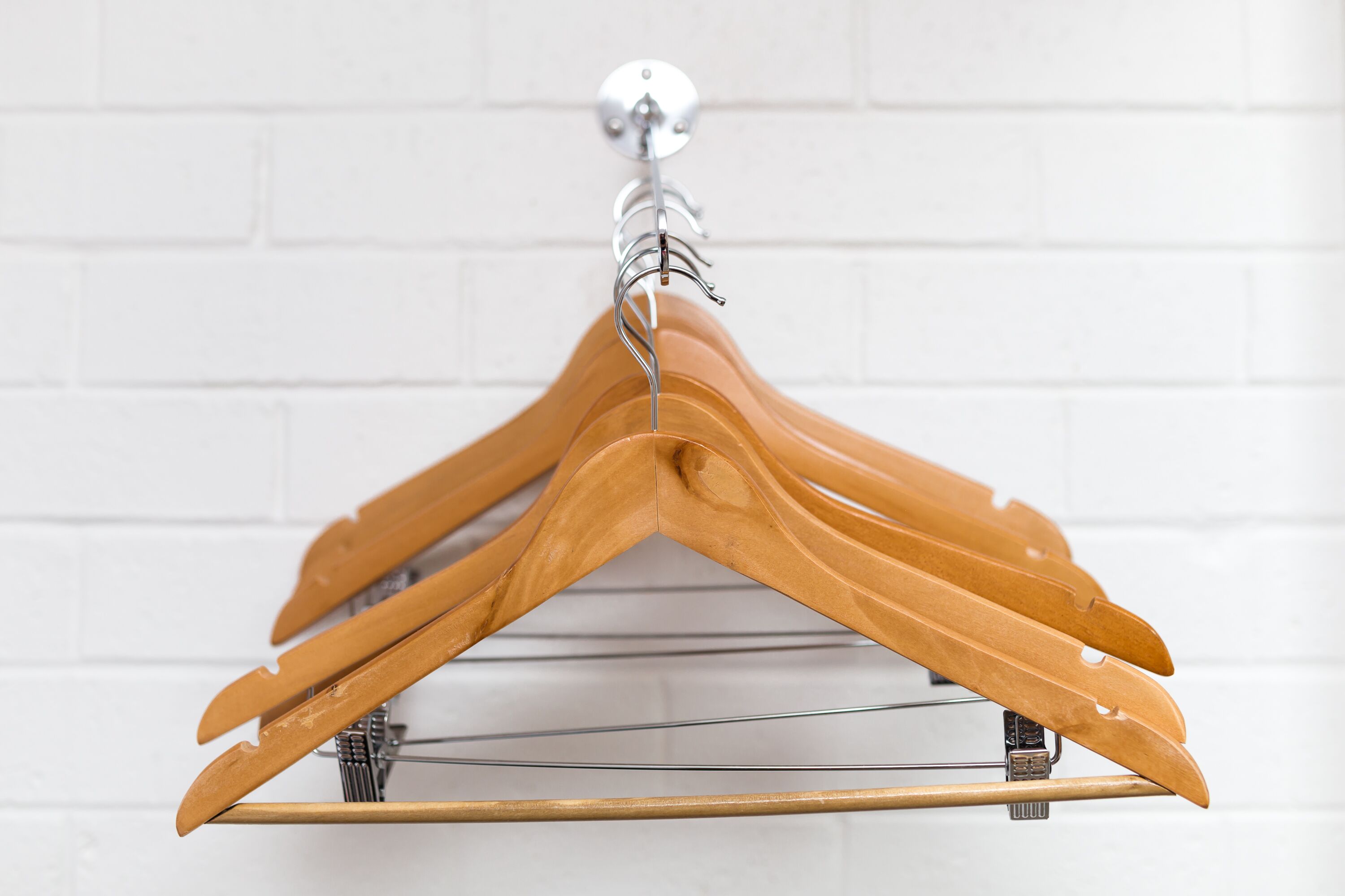 A wooden hanger rack with multiple hangers against a white brick wall.