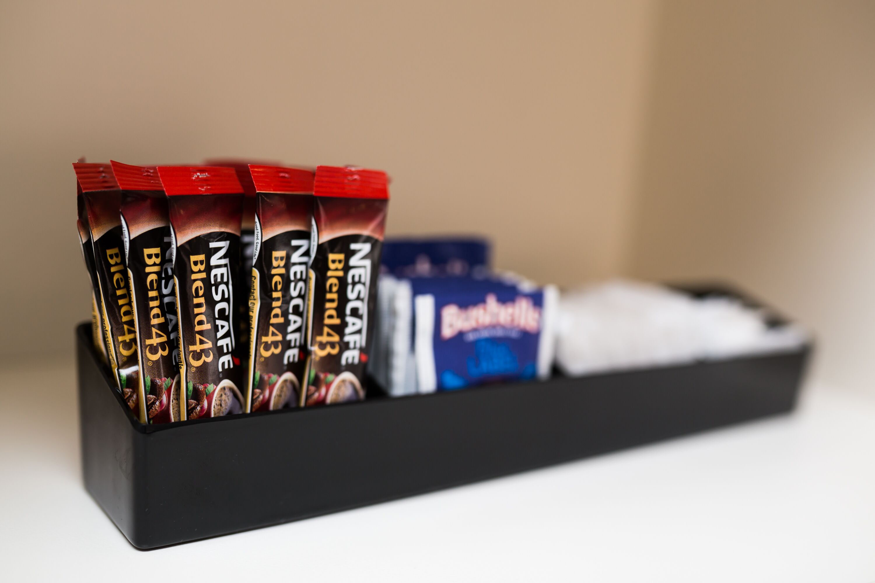 Uma bandeja preta com vários sachês de café Nestlé Blend 43 e uma caixa de chocolate Bournville.