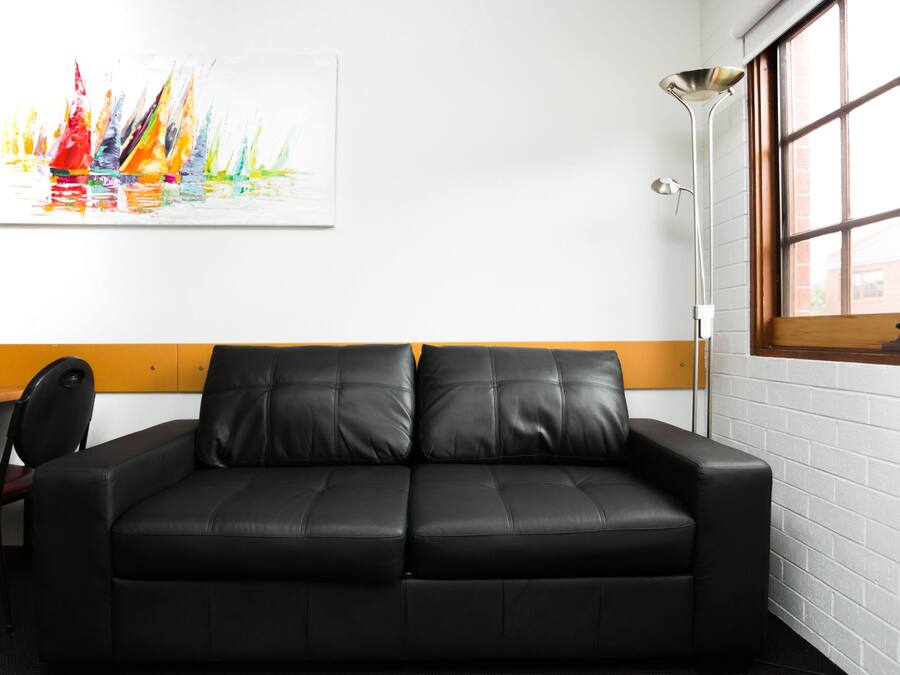 A black leather sofa with a wooden accent wall, a modern floor lamp, and a colorful abstract painting on the wall.