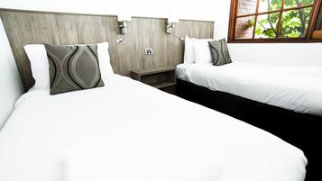 A hotel room with two beds, wooden headboards, and a window with a view of trees.