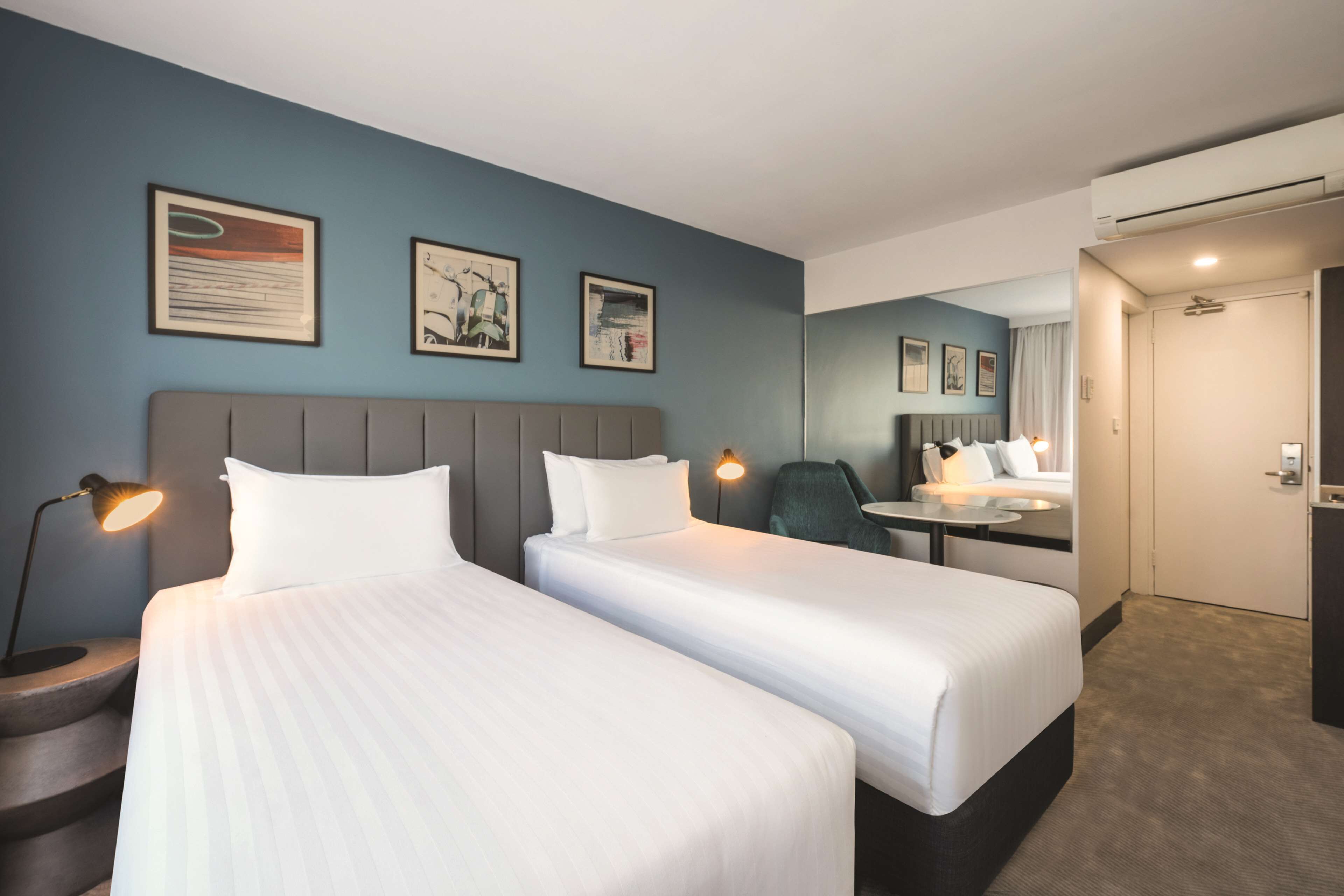 A hotel room with two beds, a desk, a chair, and a mirror.