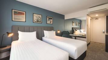 A hotel room with two beds, a desk, a chair, and a mirror.