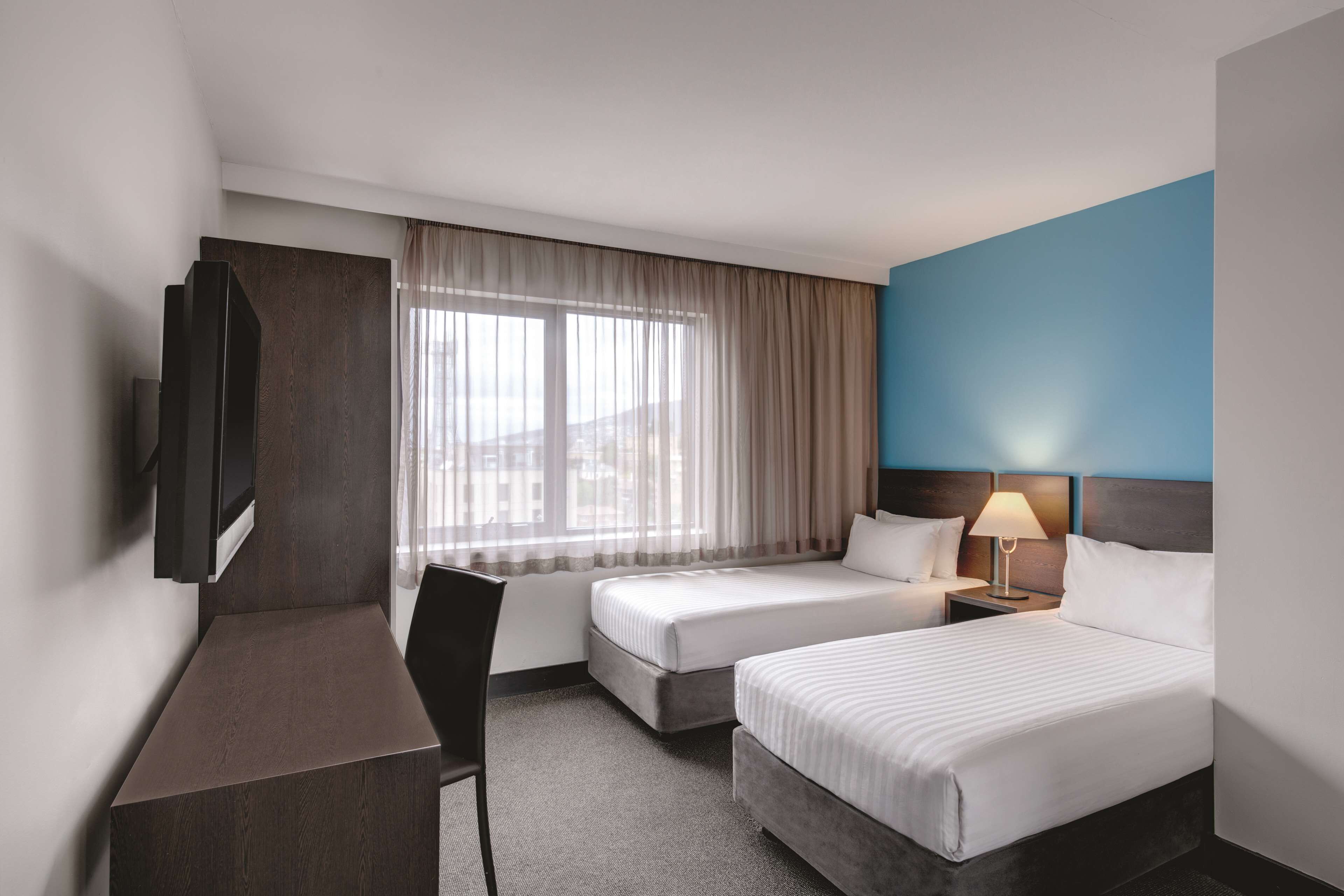 Una habitación de hotel con dos camas, un escritorio, un televisor y una ventana con cortinas.