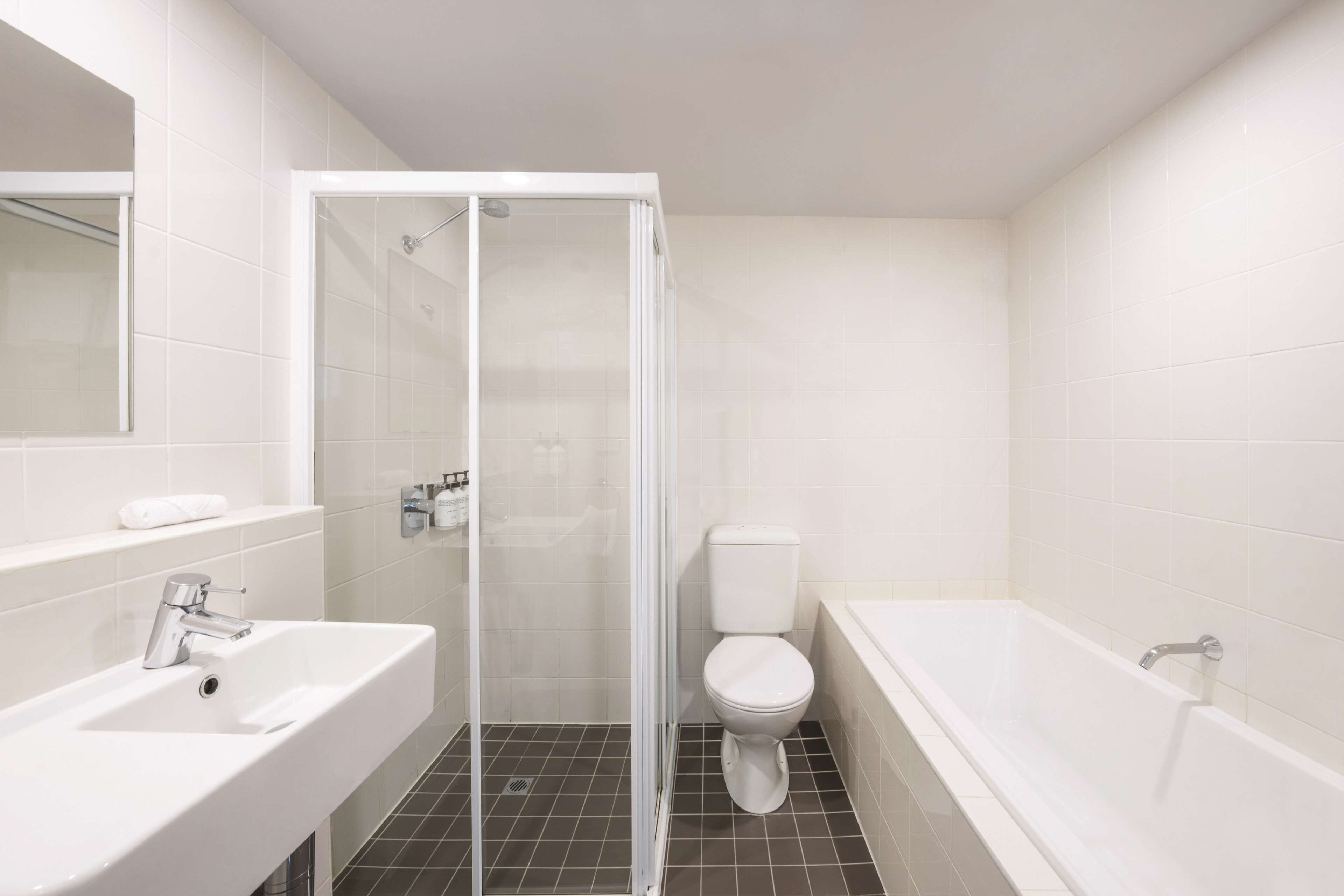 Ein modernes Badezimmer mit einer gläsernen Duschkabine, einer weißen Toilette und einer Badewanne.