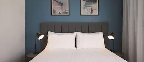 A neatly made bed with white linens, two bedside lamps, and two framed pictures on the wall.